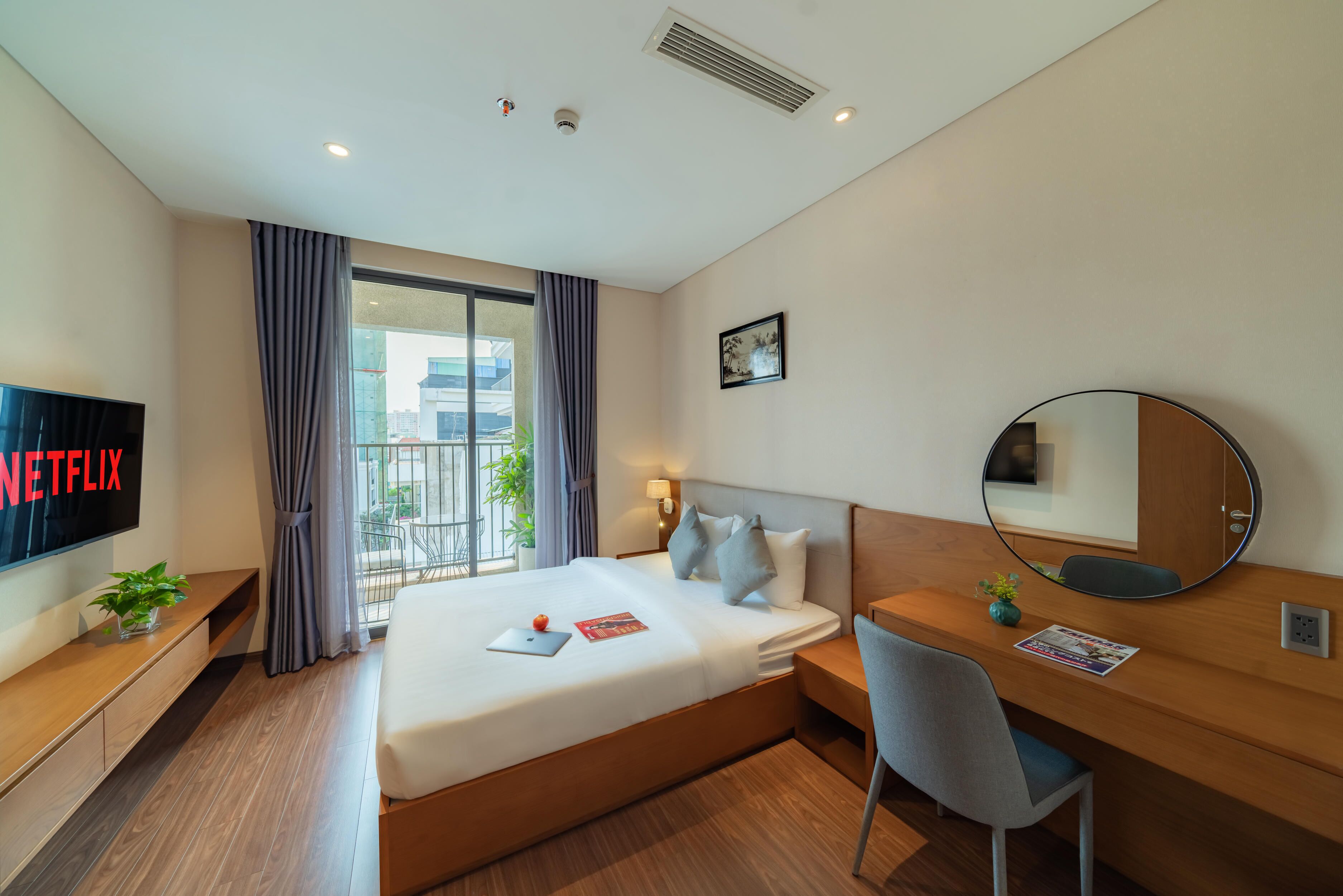 A modern hotel room with a large bed, a desk with a chair, a TV, and a window with curtains.