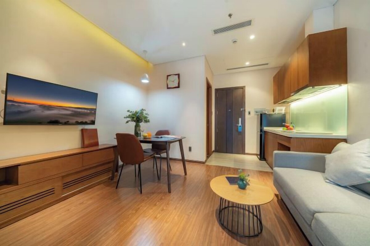 A modern living room with a wooden floor, a dining area with a table and chairs, a sofa, a coffee table, and a kitchen area with cabinets and a countertop.