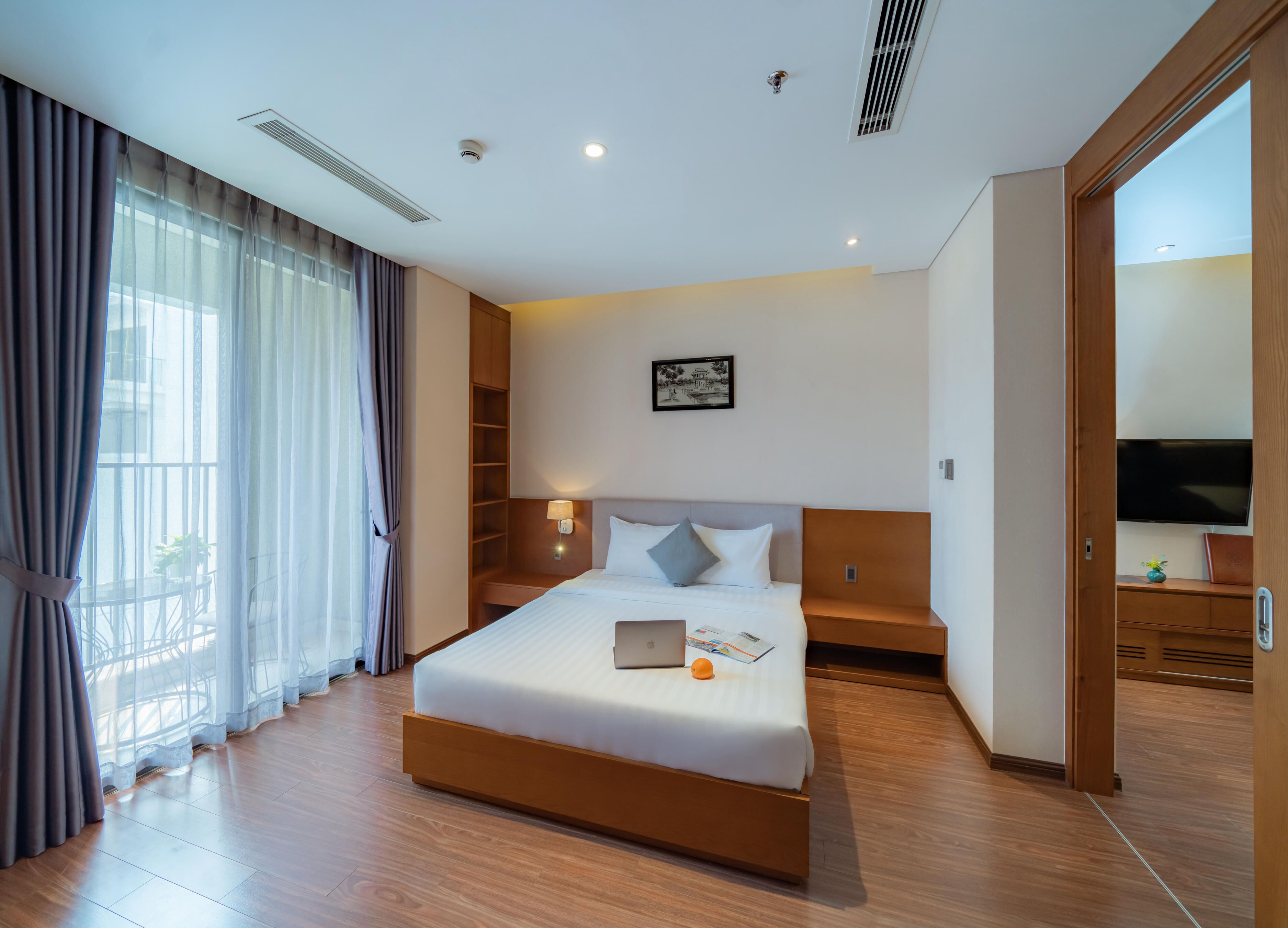 Una habitación de hotel moderna con una cama grande, una mesita de noche, un televisor y una ventana con cortinas.