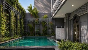 A swimming pool with a geometric fence, surrounded by greenery and a building with a modern design. - D'Primahotel Bandung (Sukajadi)