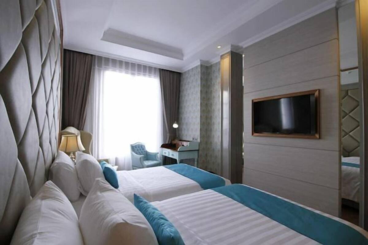 Hotellihuone, jossa on kaksi sänkyä, televisio, työpöytä ja tuoli.