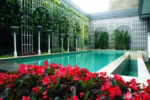 A swimming pool with a tiled edge, surrounded by lush greenery and decorative lighting. - D'Primahotel Bandung (Sukajadi)
