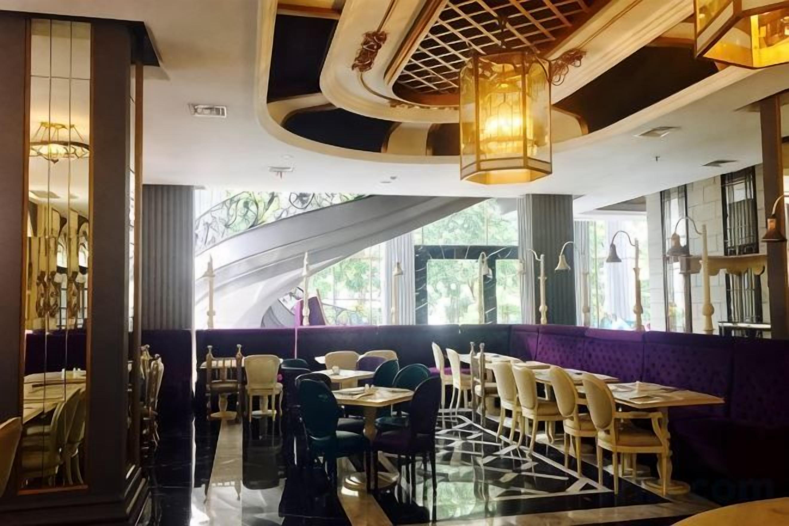 A restaurant interior with a central dining area, high ceiling with decorative elements, and large windows allowing natural light.