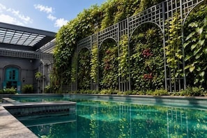 A swimming pool with a tiled deck, surrounded by a building with a green climbing wall and arched windows. - D'Primahotel Bandung (Sukajadi)