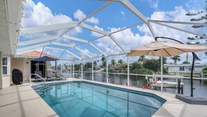 Une piscine entourée de parois en verre, avec des chaises et des parasols à l’extérieur.