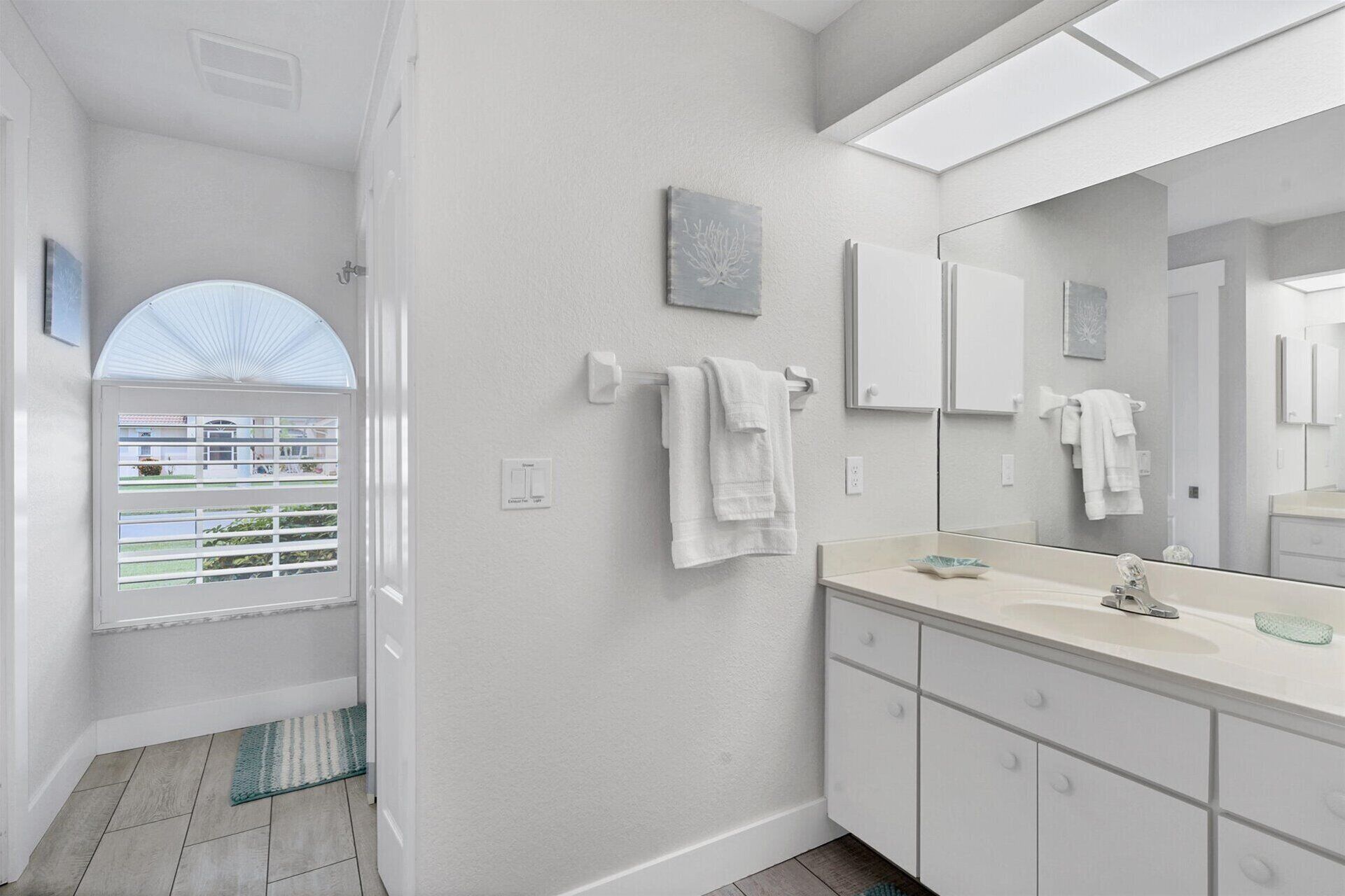 A modern bathroom with a large mirror, white cabinets, and a view through a window.