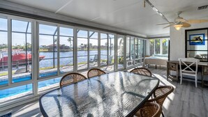 A spacious room with a large glass wall overlooking a body of water, a dining area with wicker chairs, and a ceiling fan. - Charlotte County Villa 5872: Canal-Front Private Pool Oasis (Charlotte County)