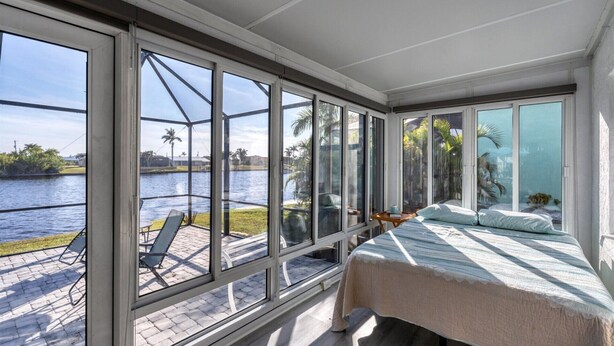 A bedroom with a large window overlooking a body of water, a bed, and a small table. - Charlotte County Villa 5872: Canal-Front Private Pool Oasis (Charlotte County)