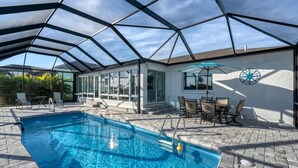 A covered swimming pool with a glass ceiling, a patio area with chairs and a table, and a wall clock. - Charlotte County Villa 5872: Canal-Front Private Pool Oasis (Charlotte County)