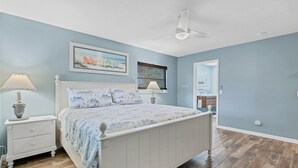 Ein Schlafzimmer mit Bett, Nachttischen, Deckenventilator und einem Fenster mit Jalousien.