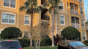 A multi-story residential building with balconies, palm trees, and a clear sky.