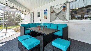 Een overdekt terras met een blauwe bank, een tafel en stoelen. Op de muur hangt een decoratief net met een vismotief.