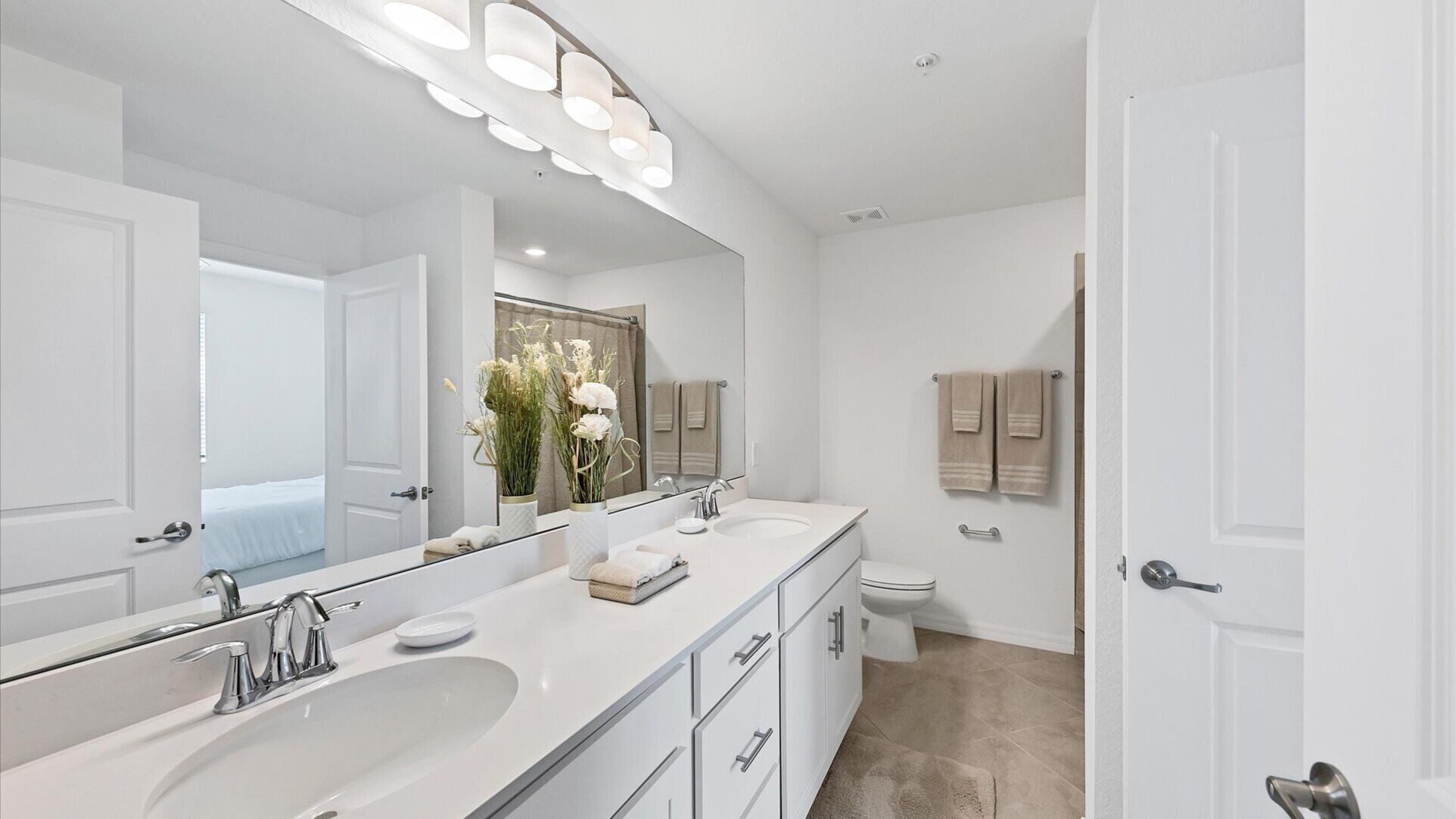A modern bathroom with a large mirror, two sinks, a toilet, and a shower area.