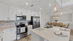 A modern kitchen with white cabinetry, stainless steel appliances, and a central island with a sink.