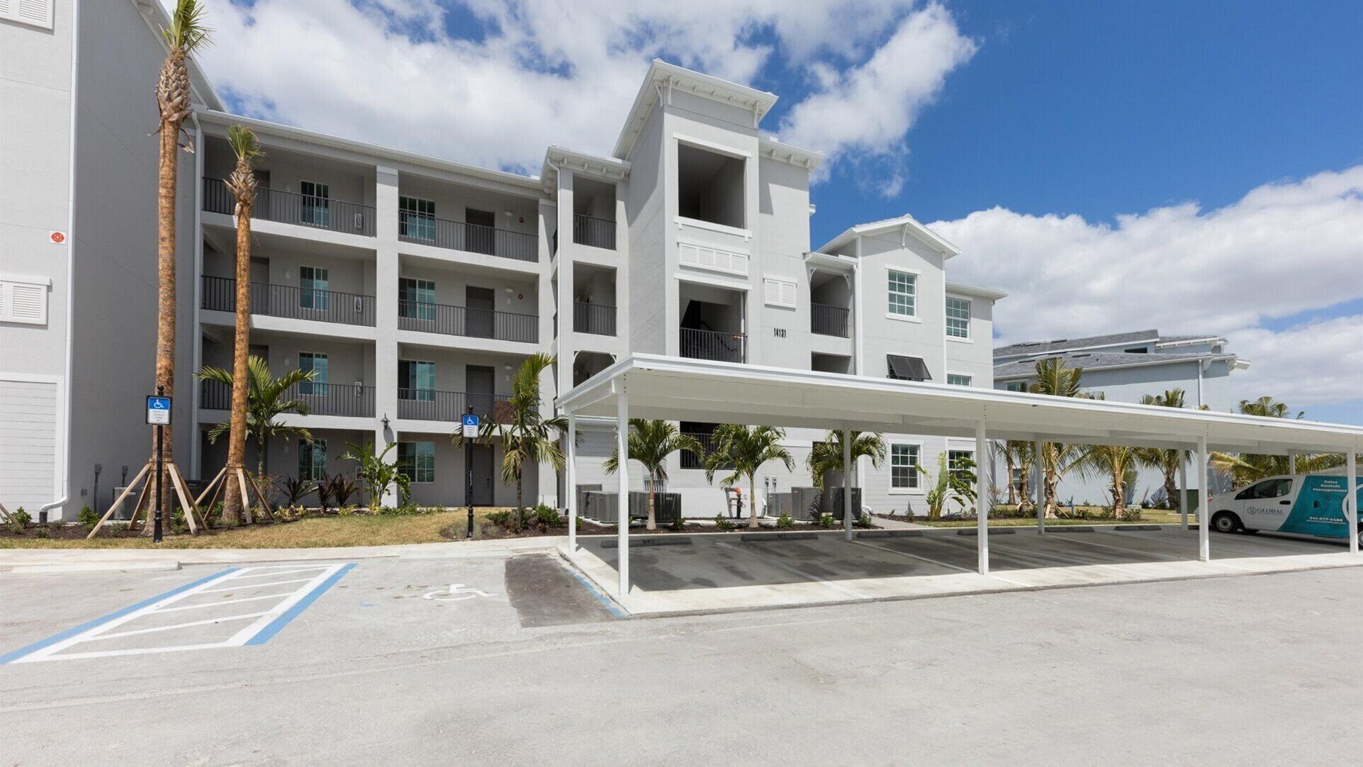 A multi-story hotel with a covered parking area, palm trees, and a clear sky.