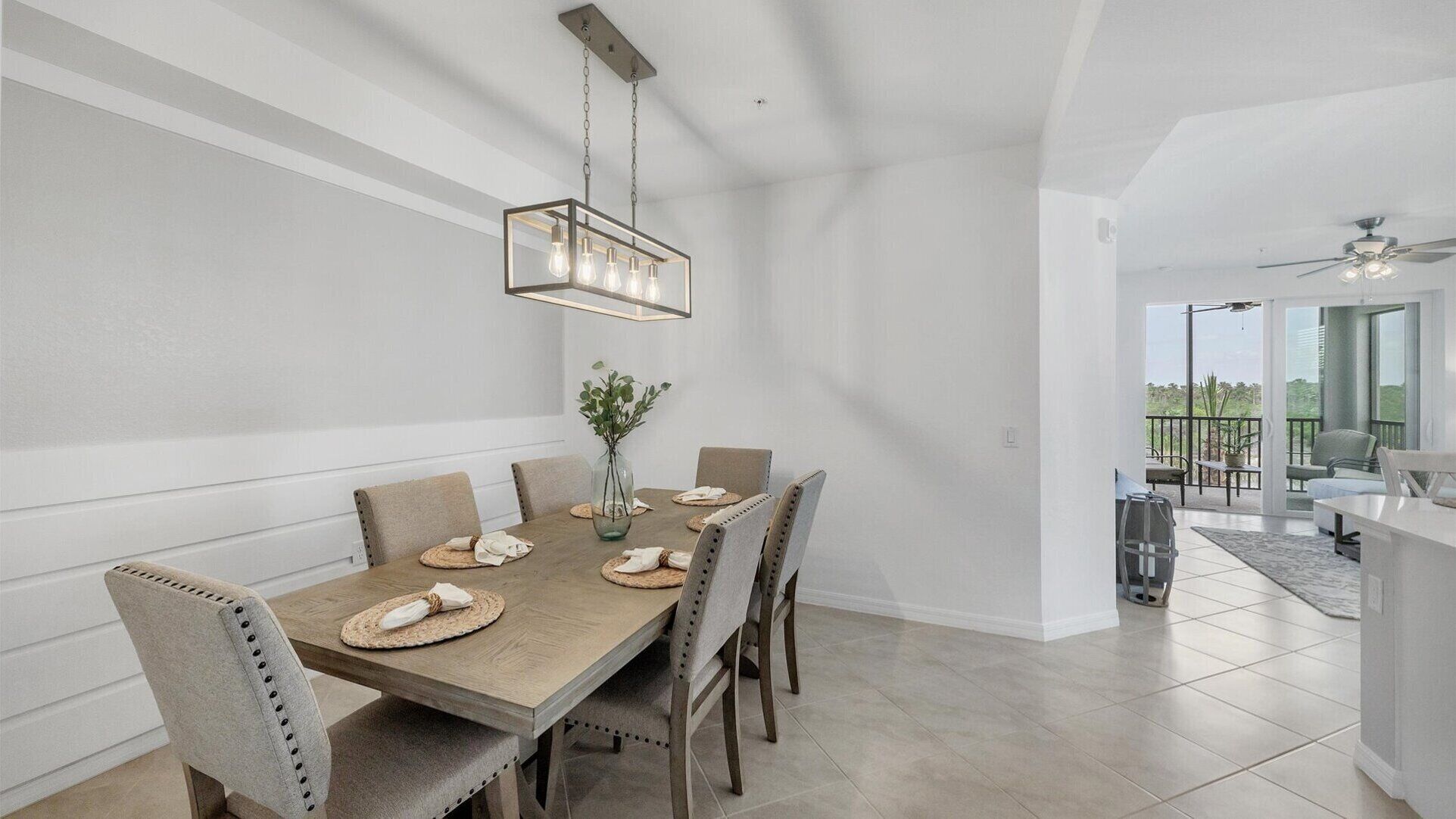 Un espace repas comprenant une table en bois, six chaises, un luminaire suspendu et une vue sur l’extérieur.