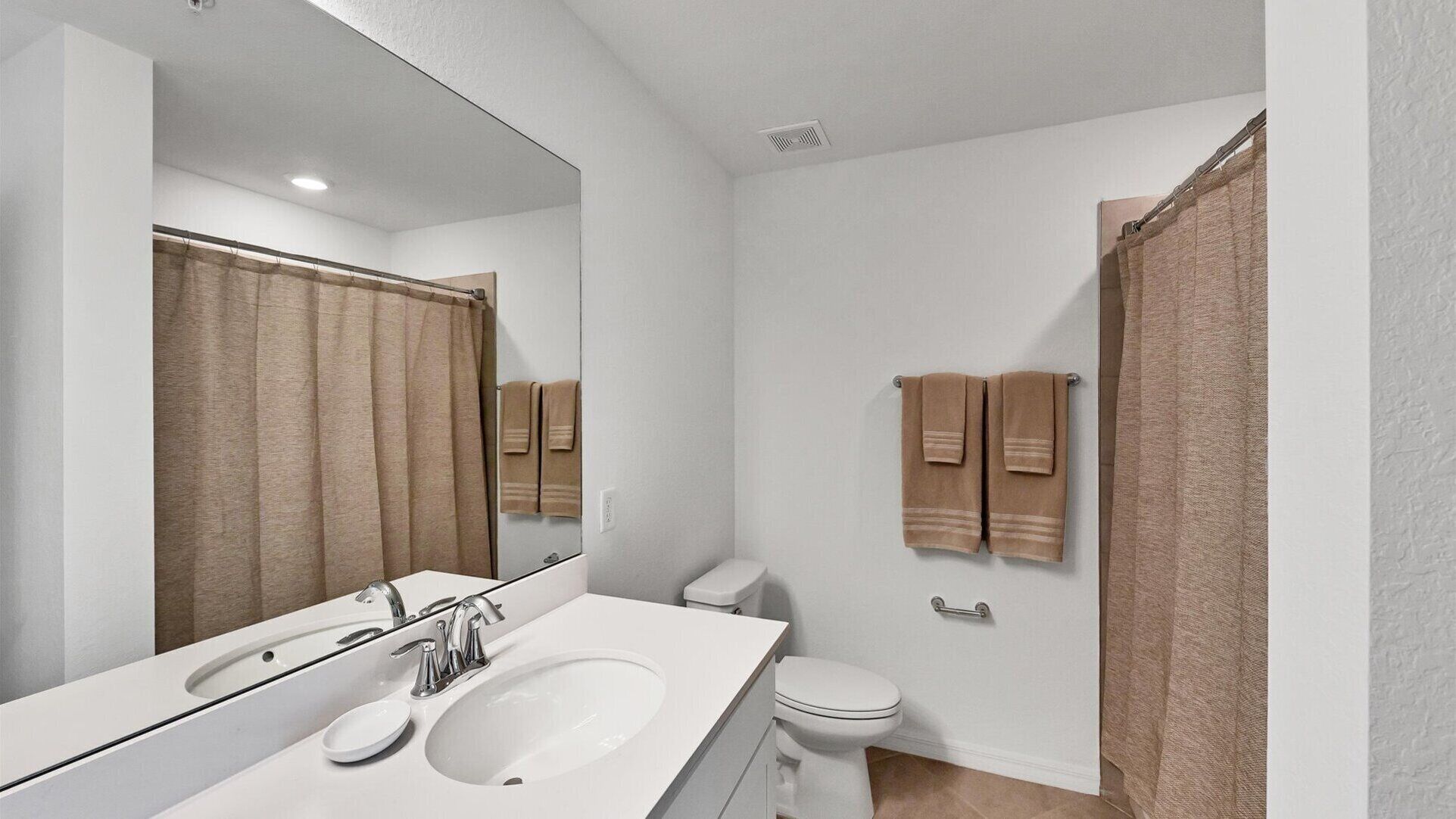 A modern bathroom with a large mirror, white sink, and toilet.
