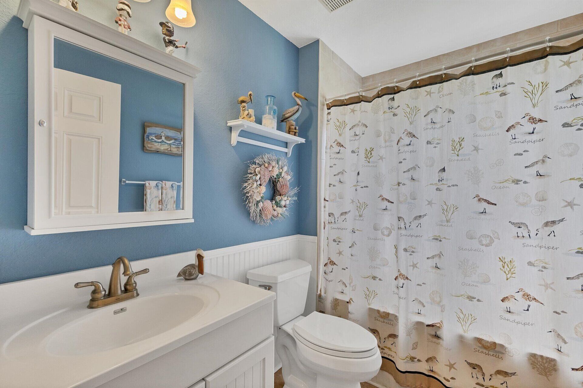 Un bagno con parete blu, sanitari bianchi, una ghirlanda decorativa e una tenda da doccia con motivi marini.