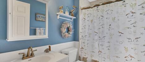 Un bagno con parete blu, sanitari bianchi, una ghirlanda decorativa e una tenda da doccia con motivi marini.