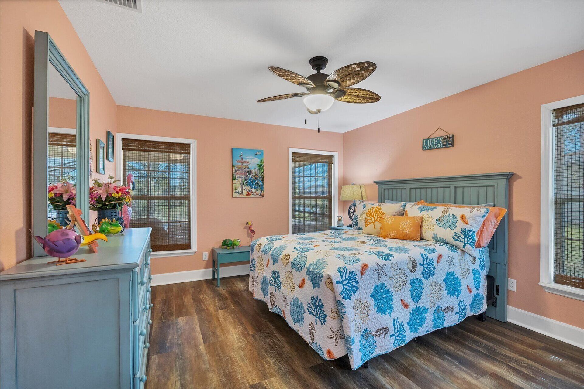 A bedroom with a bed, a dresser, a mirror, a ceiling fan, and artwork on the walls.