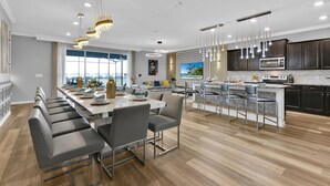 Una cocina moderna con una isla central, taburetes de bar y un comedor con una mesa larga y sillas.