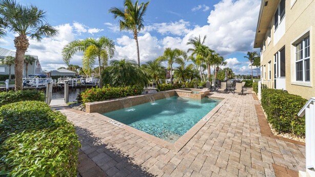 A pool area with clear water, surrounded by palm trees and a brick walkway.