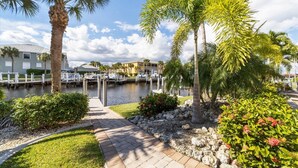 A marina with boats docked, surrounded by palm trees and a paved walkway.