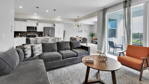 A modern living room with a grey sectional sofa, a round wooden coffee table, and a bright balcony with a view.