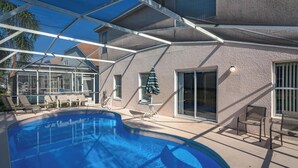 Ein Pool mit Glasveranda, Liegestühlen und einer Terrassenanlage mit Tisch und Stühlen.