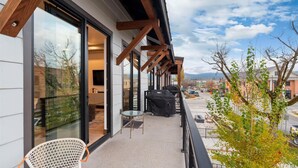 A balcony with a glass door leading to a room, a grill, and a chair. - Sunrise Escape at Downtown Whitefish (Whitefish)