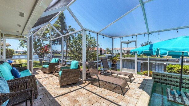 A covered outdoor area with wicker furniture, a pool, and a view of a body of water and buildings. - Charming Charlotte County Villa 5884 with Private Pool Access (Charlotte County)