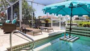 A poolside area with lounge chairs, a covered seating area, and a pool with a tiled edge. - Charming Charlotte County Villa 5884 with Private Pool Access (Charlotte County)