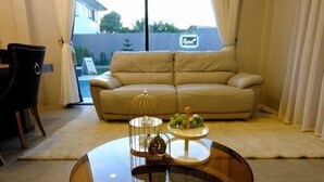 A living room with a glass coffee table, a beige sofa, and a view of a swimming pool through large windows. - Natree Pool Villa Pattaya (Pattaya)
