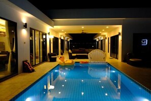 An indoor swimming pool with a clear view of the pool, a ceiling fan, and a seating area with a chair and a table. - Natree Pool Villa Pattaya (Pattaya)