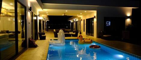 A swimming pool with a glass enclosure, a hot tub, and a lounge area with seating.