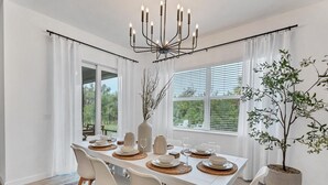 Un coin repas avec une table blanche dressée pour quatre personnes, un lustre et une plante en pot.