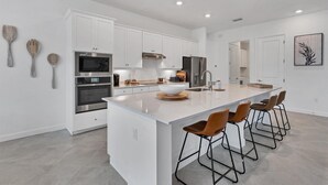 Une cuisine moderne avec des meubles blancs, des appareils en acier inoxydable et un grand îlot central doté de tabourets.