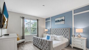 Une chambre à coucher avec un lit doté d’une tête de lit capitonnée, une table de chevet avec une lampe, une commode et une fenêtre avec des stores.