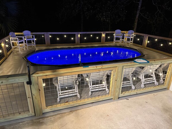 Una piscina con bordo in legno e sedie.
