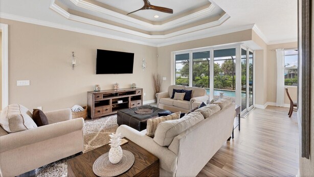 A spacious living room with a large sectional sofa, a coffee table, and a flat-screen TV mounted on the wall. There is a ceiling fan, recessed lighting, and a view of a pool through large sliding glass doors. - Private Pool & Dock, Charlotte County Villa 5890 (Charlotte County)