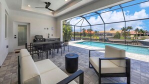 A poolside area with a glass-enclosed pool, outdoor seating, and a grill. - Charlotte County Villa 5892 - Pool Home Retreat (Charlotte County)