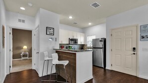 Une cuisine moderne avec des meubles blancs, des appareils en acier inoxydable et un coin bar avec des tabourets.
