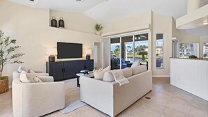 A modern living room with a flat-screen TV, two sofas, a coffee table, and a dining area with a kitchen counter.
