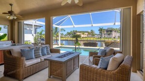 A sunlit patio with wicker furniture, a pool, and a view of a modern building and palm trees.