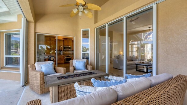A sunlit patio with wicker furniture, a glass door leading to a kitchen, and a ceiling fan.