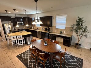 A modern kitchen with dark cabinets, a granite countertop, a central island with seating, and pendant lighting. - Charming house in The Woodlands - Creekside (Tomball)
