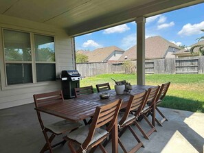A covered patio with a wooden table and chairs, a grill, and a potted plant. - Charming house in The Woodlands - Creekside (Tomball)
