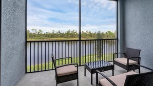 A balcony with a view of a lake and trees, furnished with wicker chairs and a glass table. - Condo 5896 at Heritage Landing: Relax & Unwind Here (Charlotte County)