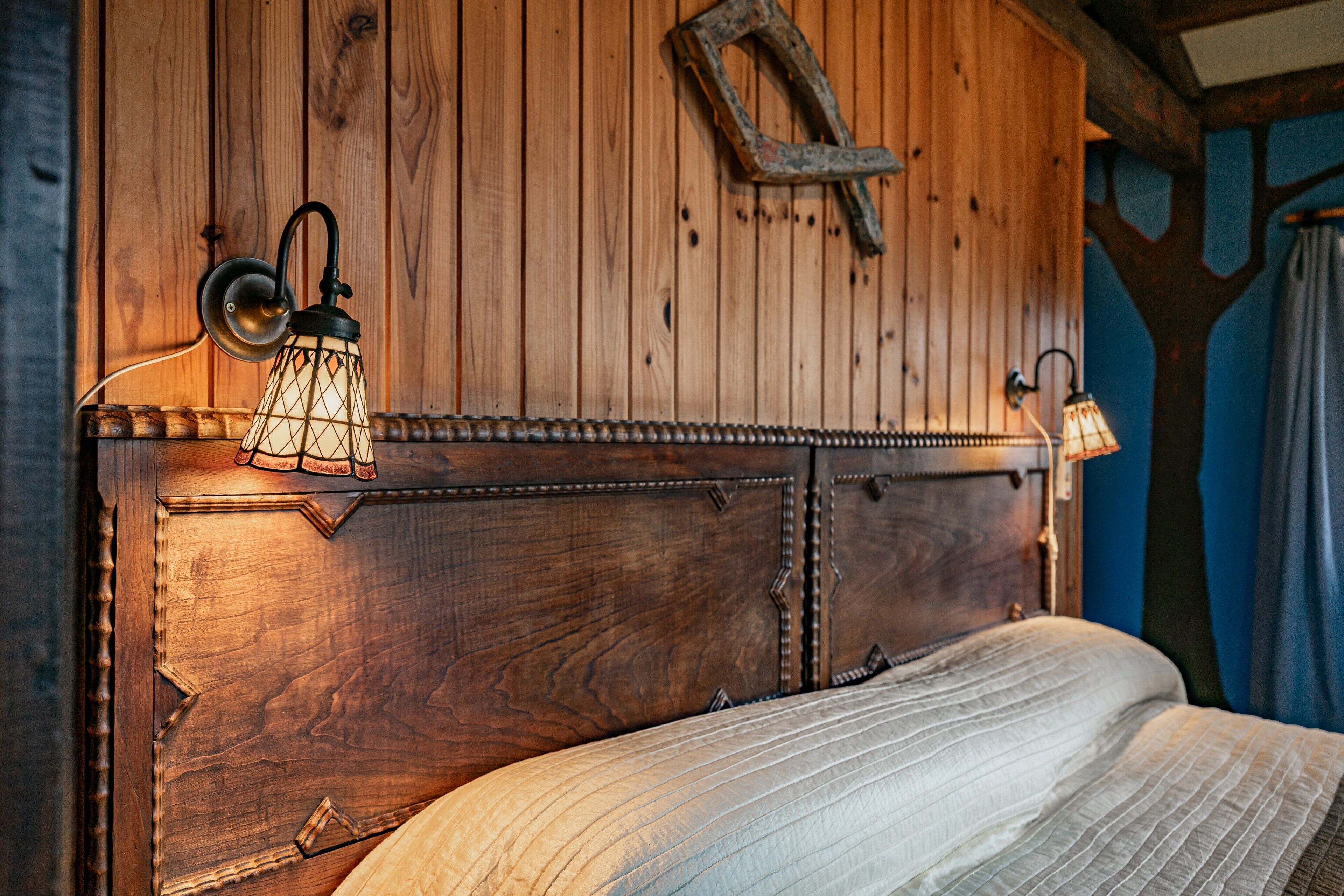 Cabecera de madera con cama, dos lámparas fijadas a la pared y un adorno rústico en la pared.