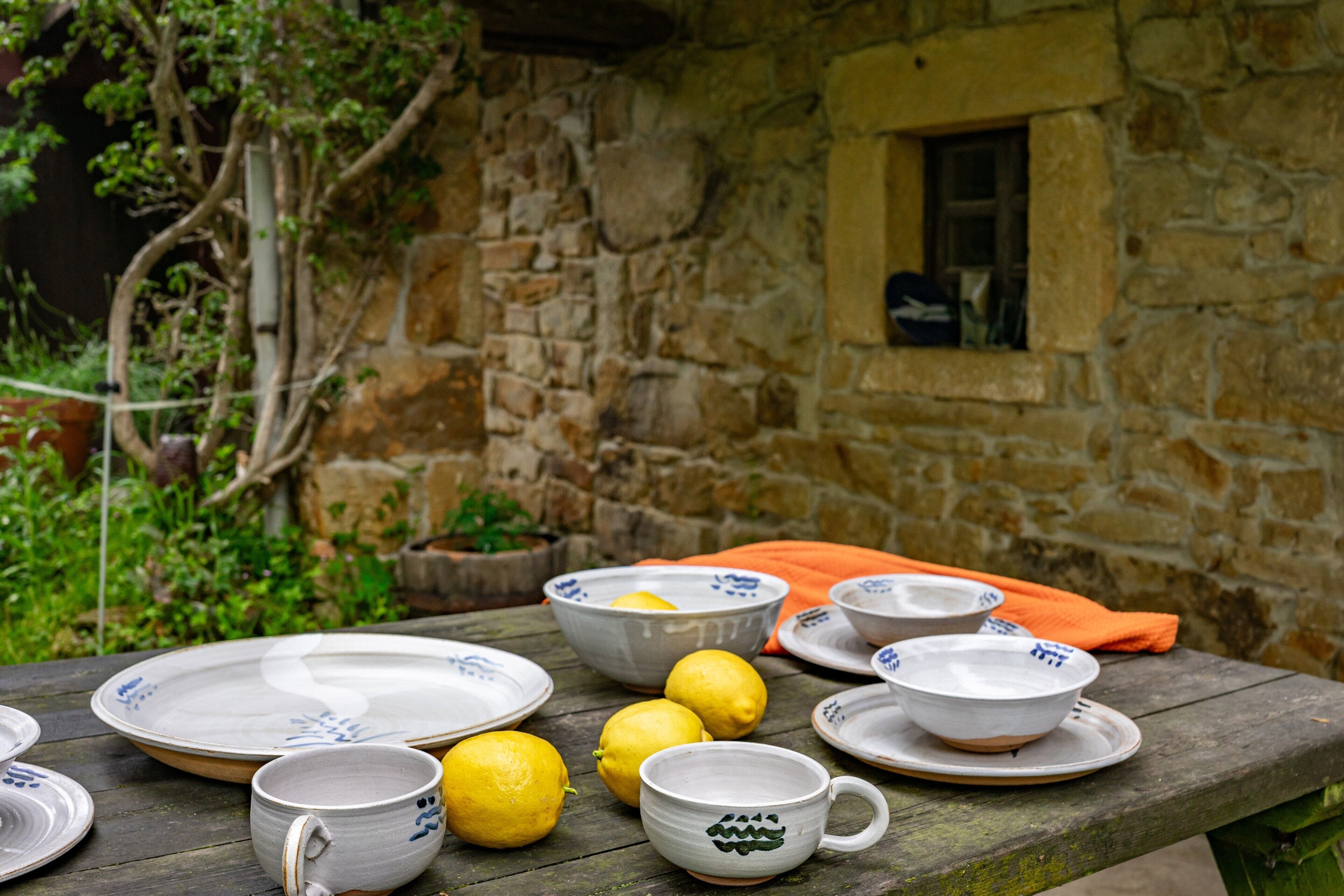 Una mesa de comedor rústica al aire libre con platos de cerámica, tazas y limones.